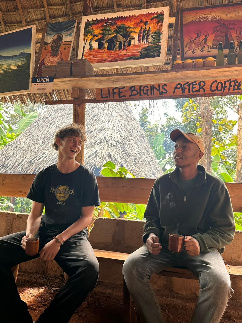 Travelers sharing coffee with a local guide under a thatched roof